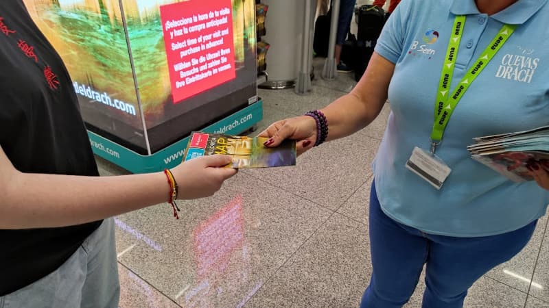 Stand de las Cuevas del Drach en el aeropuerto de Palma, donde se ve a la azafata del stand entregando un mapa.