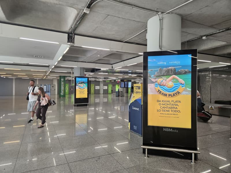 Dos mupis digitales mostrando ambos un anuncio de Vueling, cerca de las cintas de recogida de equipaje del aeropuerto de Palma.